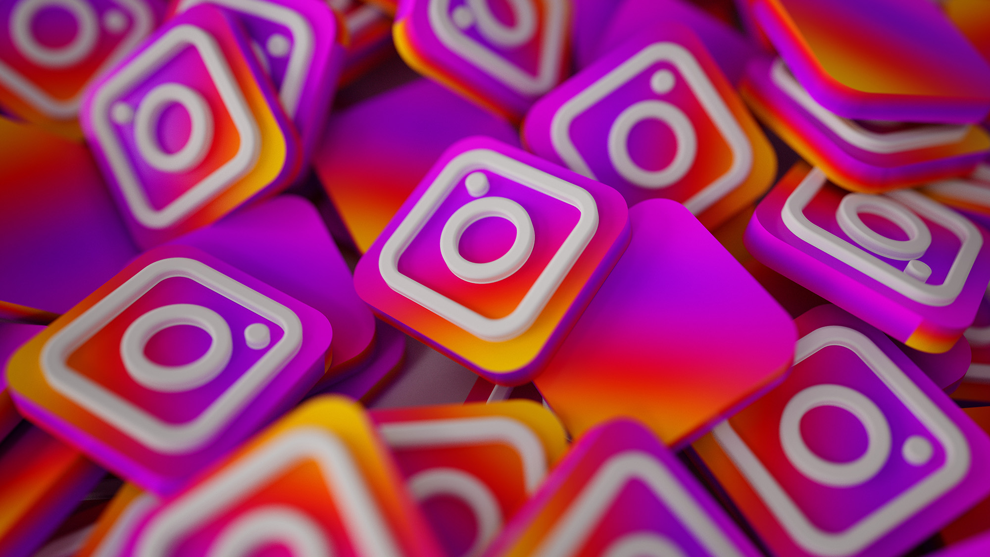 Ein Stapel 3D-Instagram-Logos mit einem weißen Kamerasymbol auf einem leuchtend pink-, orange- und lilafarbenen Hintergrund mit Farbverlauf.